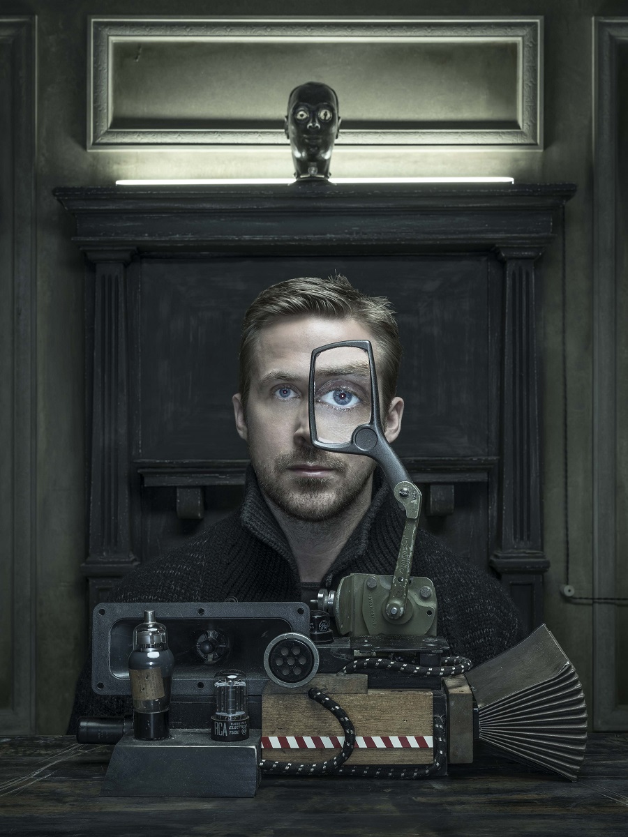Man sits behind machine with magnifying glass in front of one eye, enlarging it, in front of architectural details and lit-up doll's head